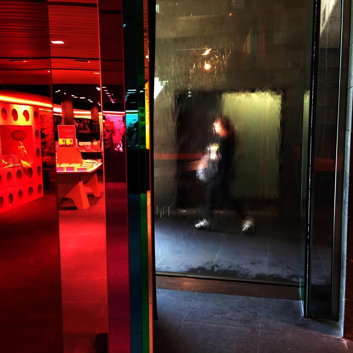 behind a wall of water a woman walks out of a building towards a bright red bookstore