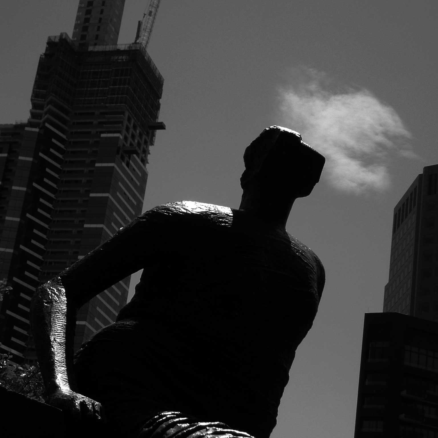massive primitive sculpture backlit by sun and in the sky tall buildings under construction