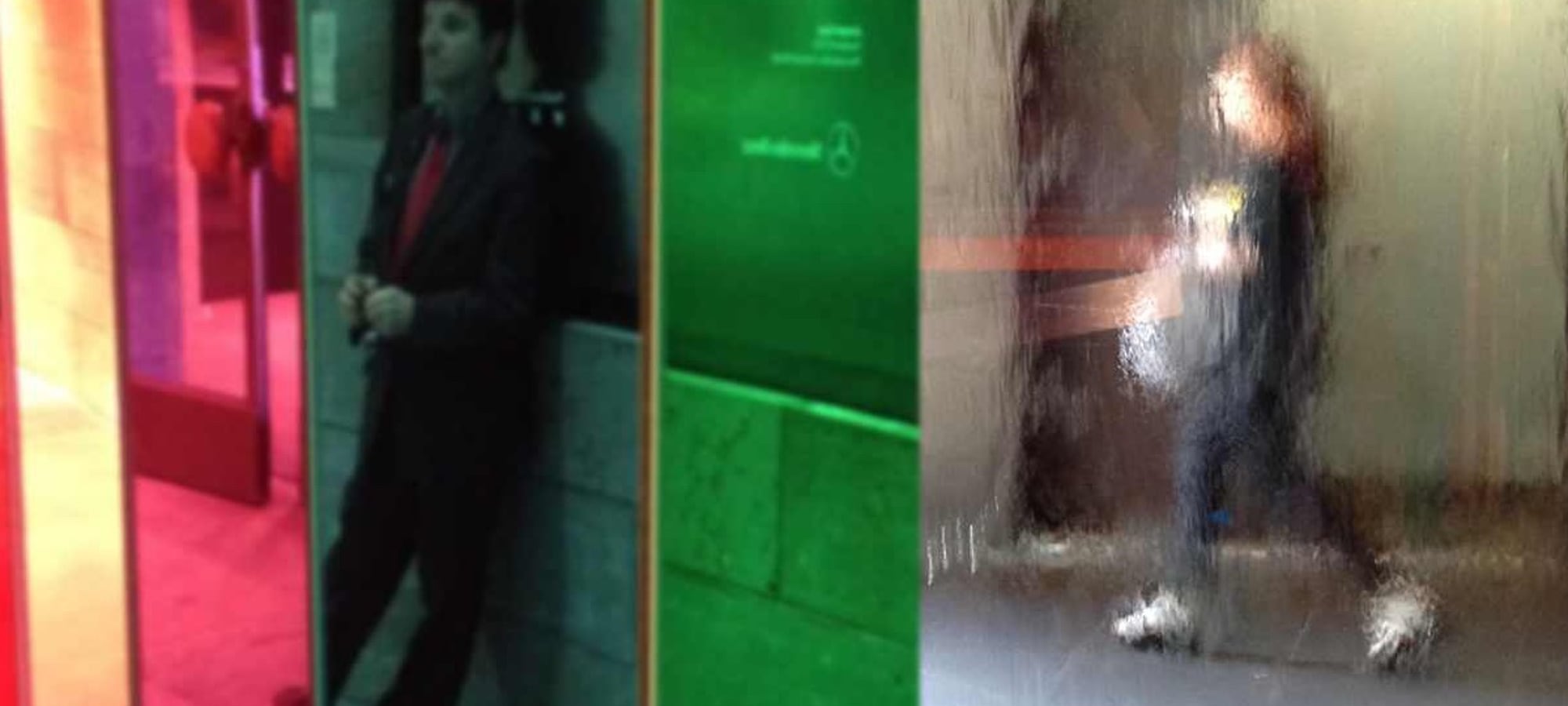 behind glass a man leans against a wall a woman walks away
