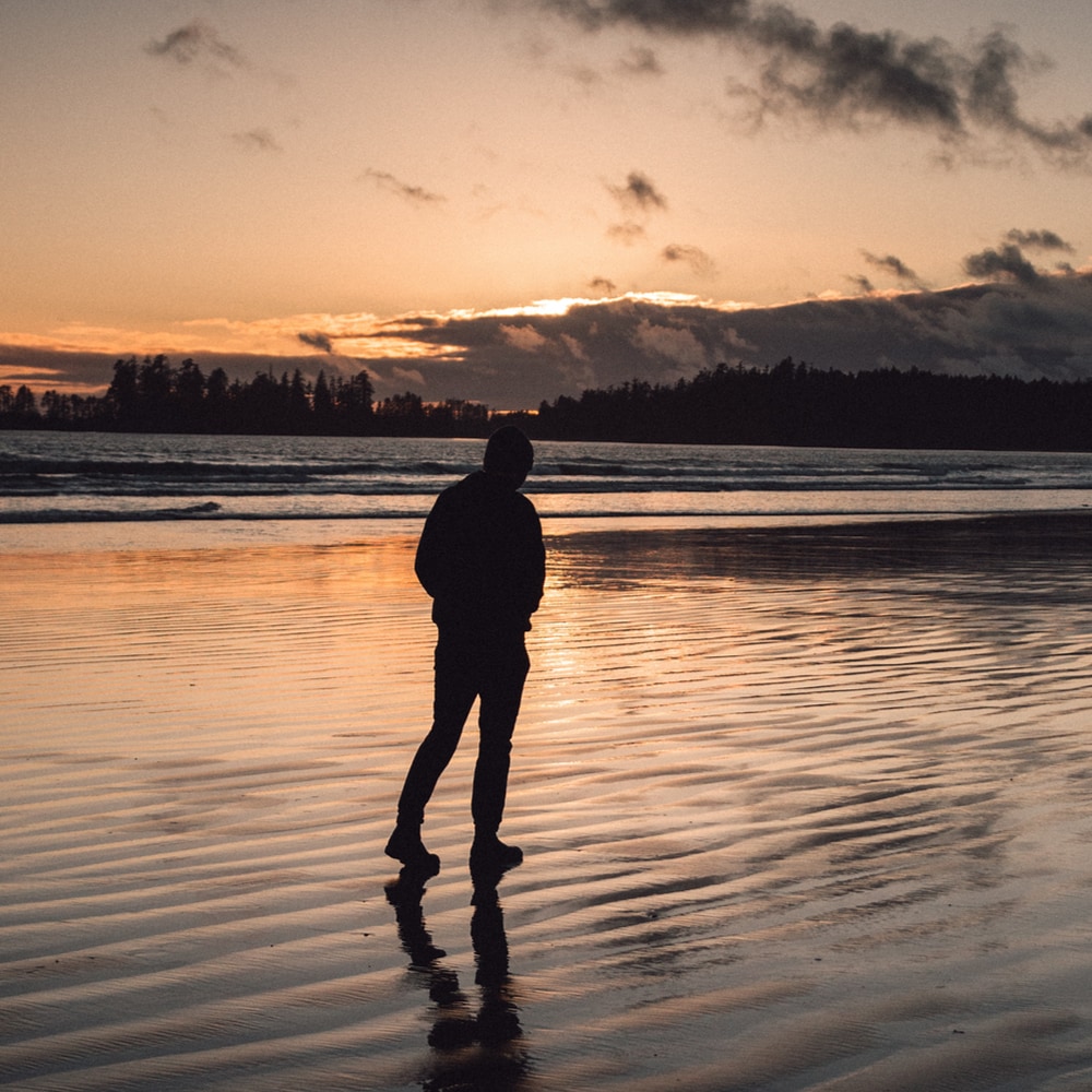 silhouette of man walking on beach, wet sand, sunset