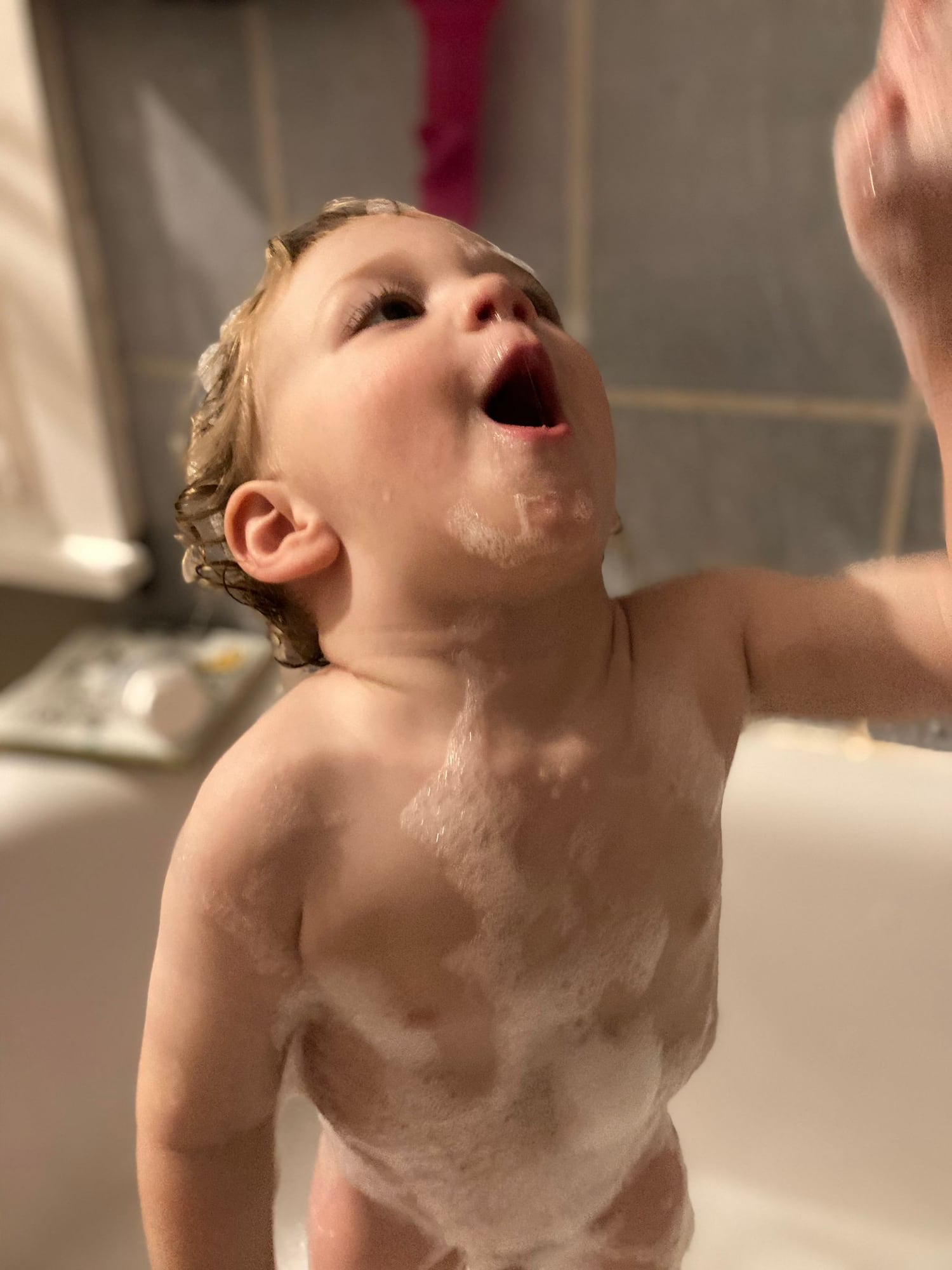 toddler stands in bath and reaches up